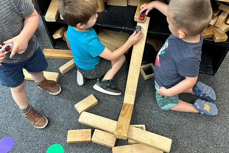 Kids racing toy cars down wooden blocks.