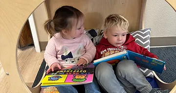 Two toddlers reading books on a couch